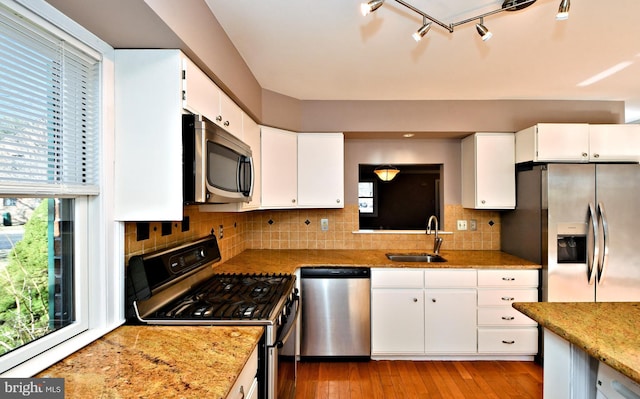 kitchen with light wood-style flooring, a sink, decorative backsplash, appliances with stainless steel finishes, and white cabinetry