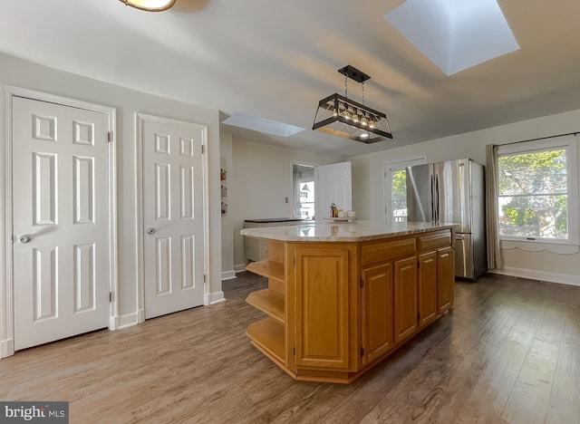 kitchen featuring open shelves, light stone counters, wood finished floors, freestanding refrigerator, and a skylight