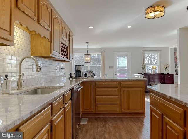 kitchen with a sink, stainless steel dishwasher, wood finished floors, a peninsula, and light stone countertops