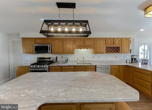 kitchen featuring light stone counters, a sink, decorative backsplash, appliances with stainless steel finishes, and pendant lighting