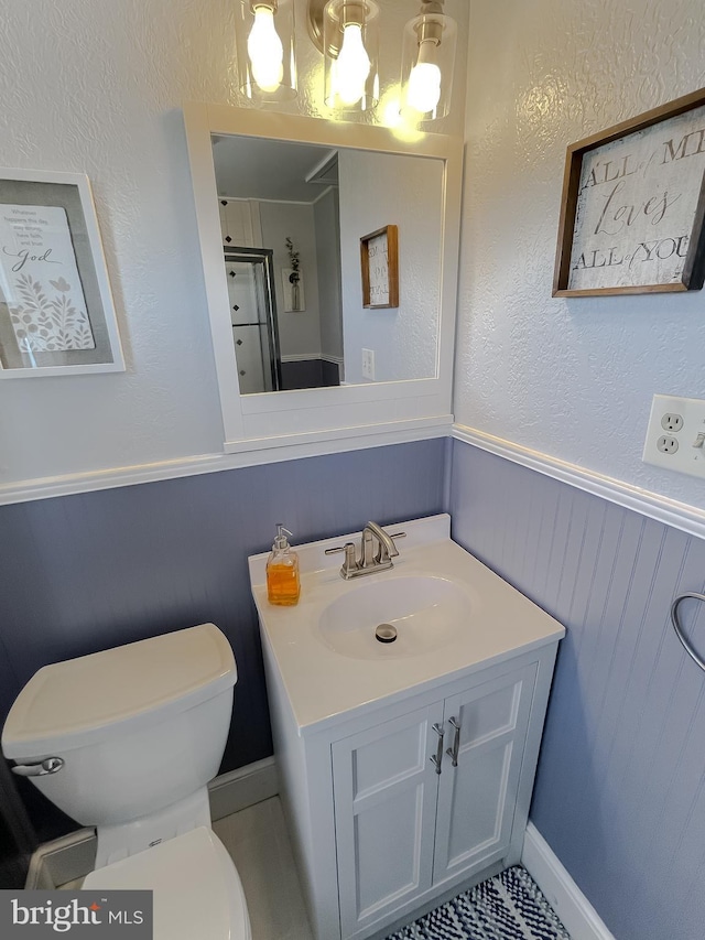 bathroom with toilet, walk in shower, wainscoting, and vanity