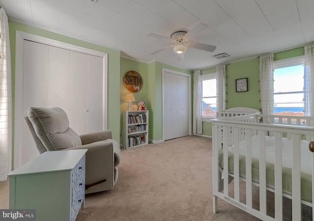 bedroom featuring visible vents, multiple closets, light carpet, a ceiling fan, and a nursery area