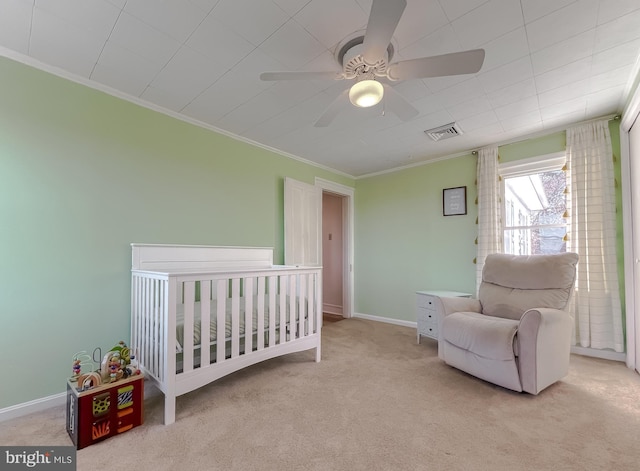 carpeted bedroom with visible vents, a crib, crown molding, baseboards, and a ceiling fan