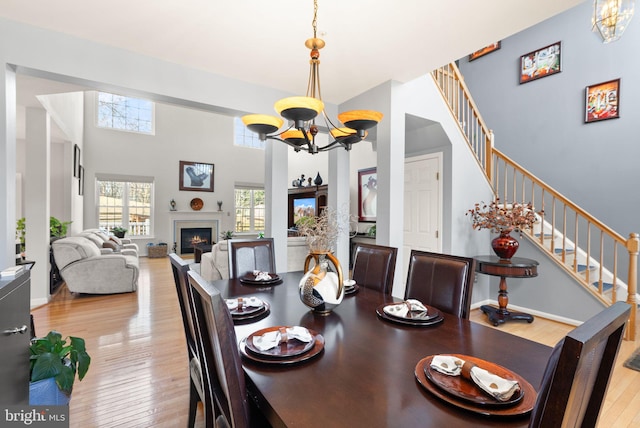 dining space featuring stairway, an inviting chandelier, a lit fireplace, hardwood / wood-style flooring, and a towering ceiling