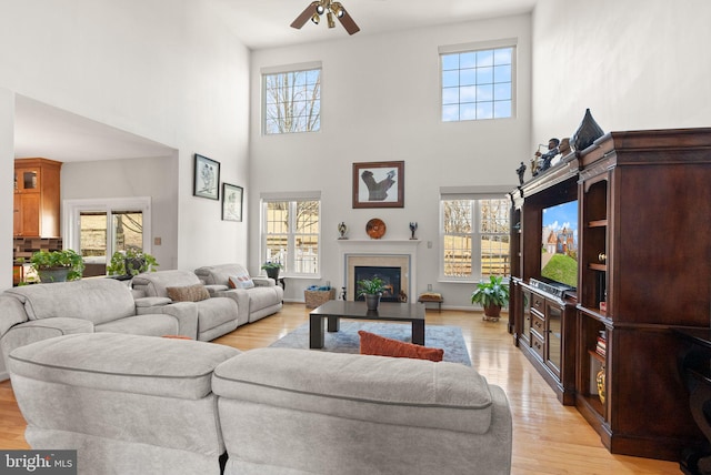 living room featuring light wood-style flooring, a fireplace, baseboards, and ceiling fan