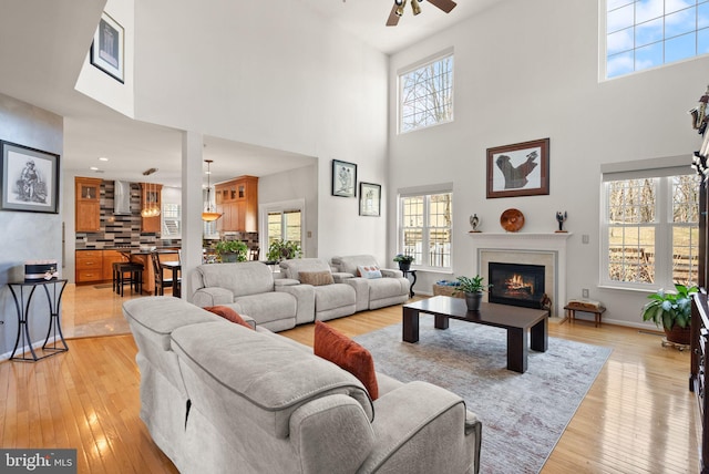 living room featuring light wood-style flooring, baseboards, a lit fireplace, and ceiling fan