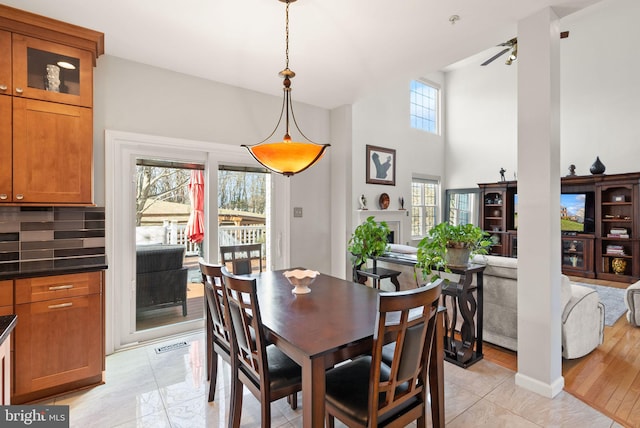 dining space with a fireplace, a ceiling fan, visible vents, and a towering ceiling