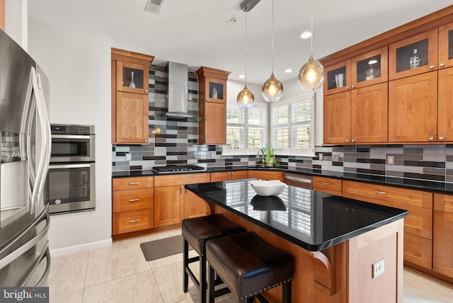 kitchen featuring decorative backsplash, brown cabinets, a kitchen breakfast bar, stainless steel appliances, and wall chimney exhaust hood