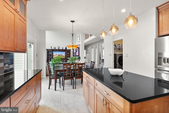 kitchen featuring a center island with sink, washer / dryer, dark stone counters, glass insert cabinets, and stainless steel refrigerator with ice dispenser