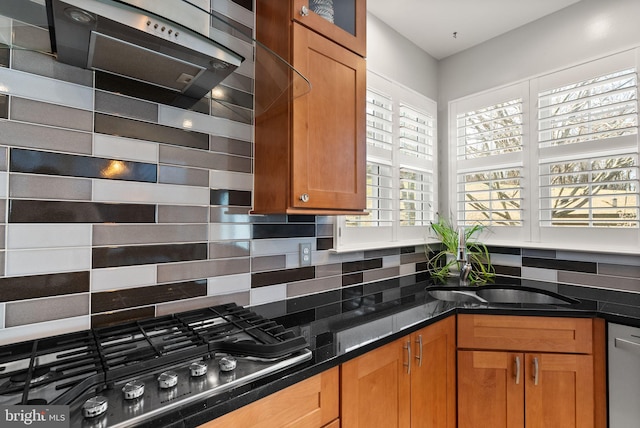 kitchen featuring tasteful backsplash, brown cabinets, dark stone countertops, stainless steel appliances, and a sink