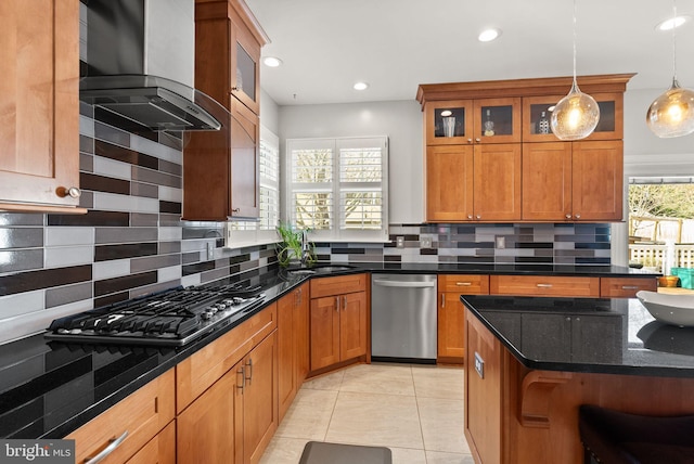 kitchen with brown cabinetry, light tile patterned flooring, a sink, stainless steel appliances, and wall chimney range hood