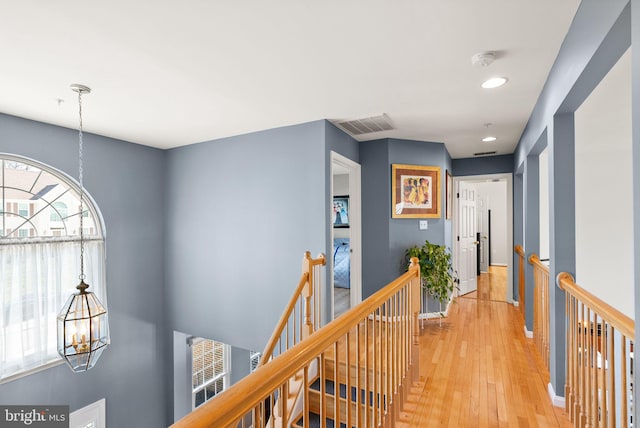 corridor featuring light wood-style floors, a notable chandelier, an upstairs landing, and visible vents