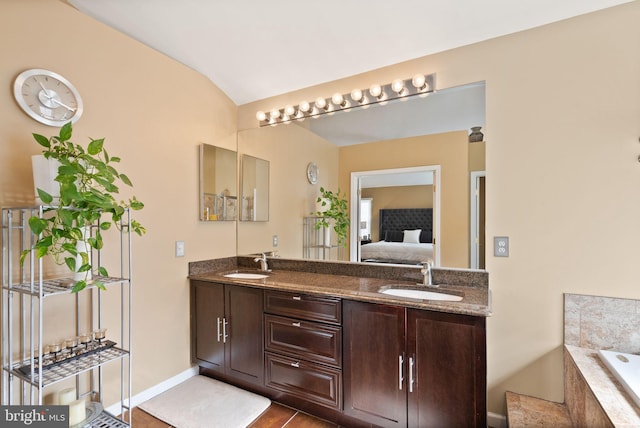 ensuite bathroom with double vanity, connected bathroom, a relaxing tiled tub, and a sink