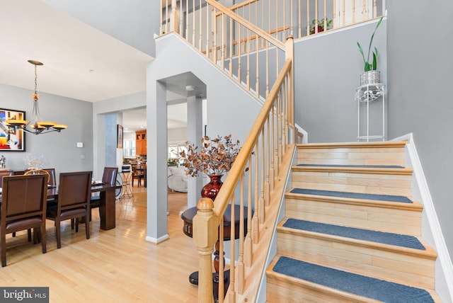 stairs with baseboards, a notable chandelier, wood finished floors, and a towering ceiling