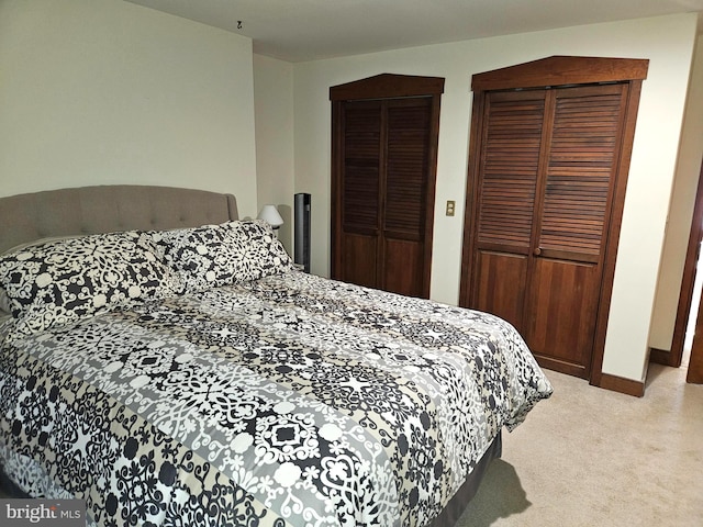 bedroom with light carpet, two closets, and baseboards