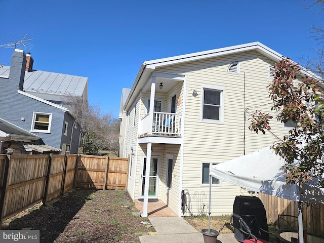 rear view of property featuring a balcony and a fenced backyard