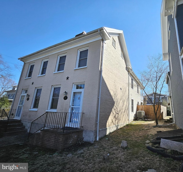 view of front of property with brick siding, central AC unit, and fence