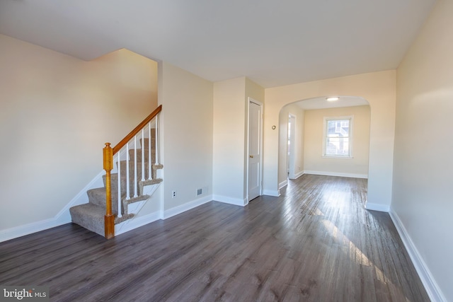 interior space featuring dark wood finished floors, arched walkways, stairs, and baseboards