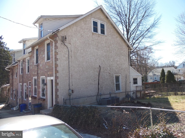 view of property exterior with central AC unit, fence, and stucco siding