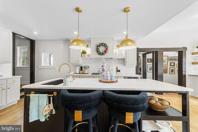 kitchen with white cabinetry, light wood-style floors, backsplash, and a sink