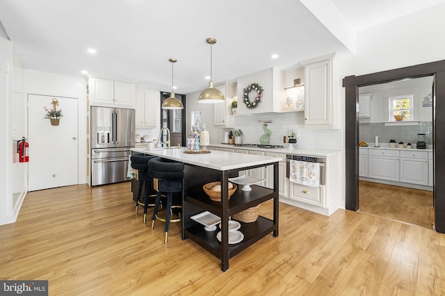 kitchen with stainless steel appliances, light countertops, white cabinetry, a kitchen breakfast bar, and light wood-type flooring