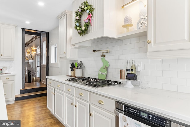 kitchen featuring light wood-style flooring, backsplash, white cabinets, dishwashing machine, and stainless steel gas cooktop