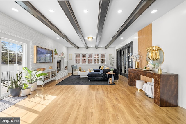 living area with brick wall, light wood-style floors, french doors, beamed ceiling, and a large fireplace