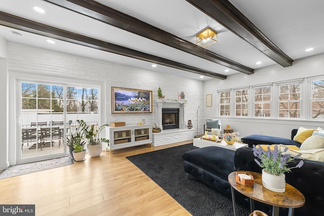 living area featuring brick wall, a large fireplace, beamed ceiling, recessed lighting, and wood finished floors