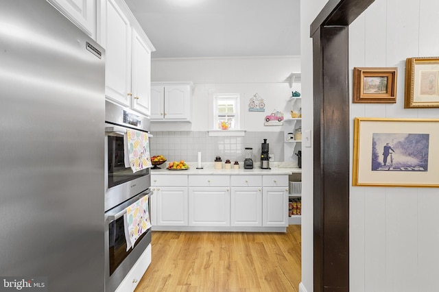 kitchen with backsplash, stainless steel appliances, light wood-style floors, white cabinets, and light countertops