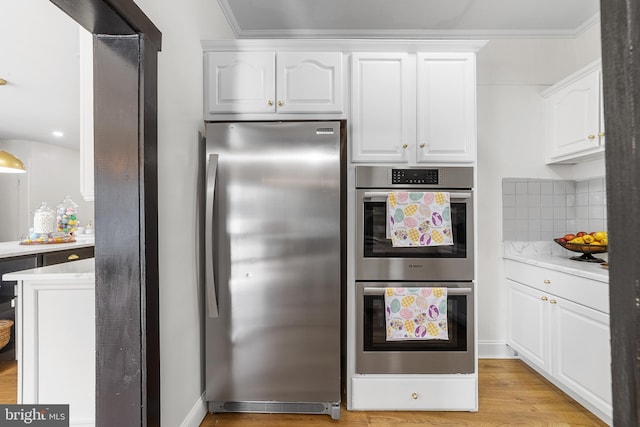 kitchen featuring tasteful backsplash, appliances with stainless steel finishes, white cabinets, light wood finished floors, and light countertops