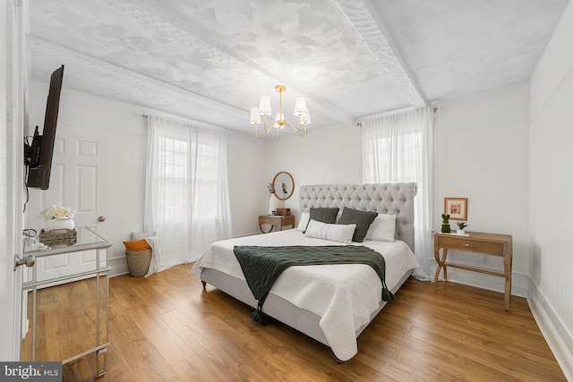 bedroom featuring a chandelier, beam ceiling, multiple windows, and hardwood / wood-style floors