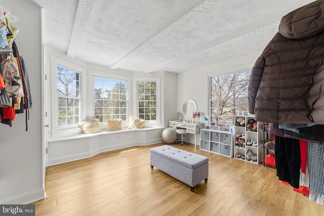 recreation room with beamed ceiling, wood-type flooring, plenty of natural light, and a textured ceiling