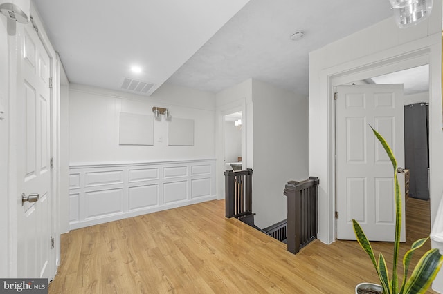 corridor with an upstairs landing, visible vents, and light wood finished floors