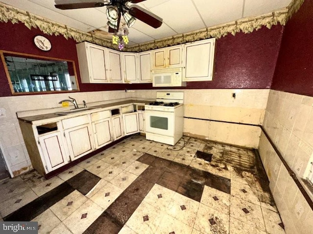 kitchen featuring a wainscoted wall, a sink, white appliances, tile walls, and ceiling fan