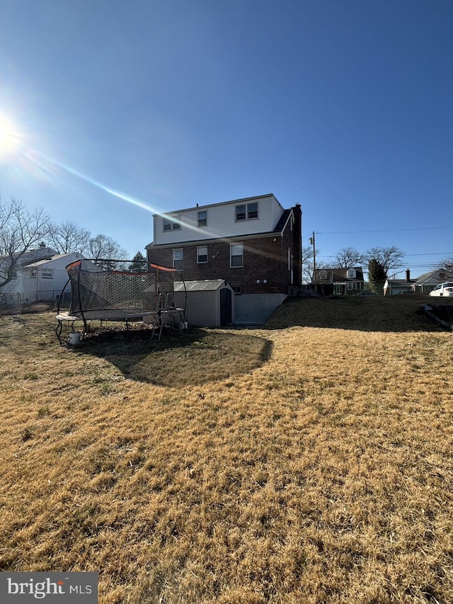 rear view of property featuring a storage unit, a yard, an outbuilding, and a trampoline