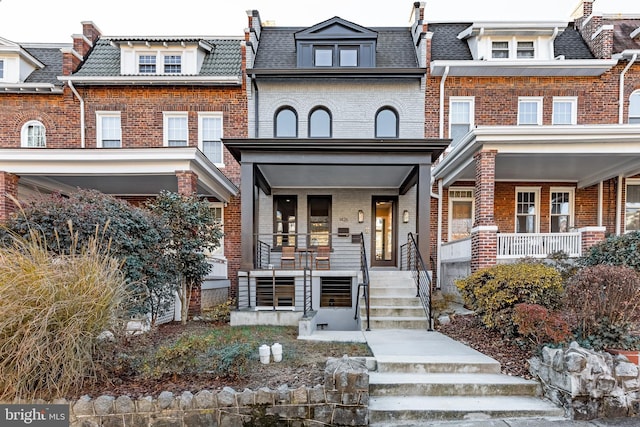 view of front facade featuring brick siding, covered porch, and mansard roof