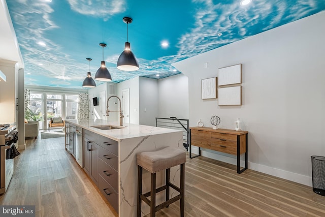 kitchen featuring light stone countertops, baseboards, stainless steel appliances, a sink, and light wood-type flooring