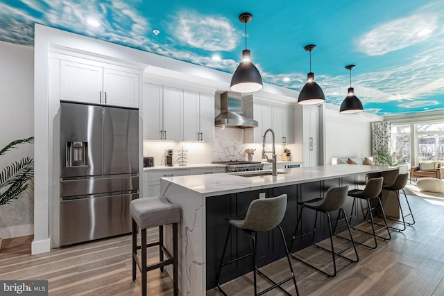 kitchen featuring light wood-style flooring, stainless steel fridge with ice dispenser, a sink, white cabinetry, and wall chimney exhaust hood