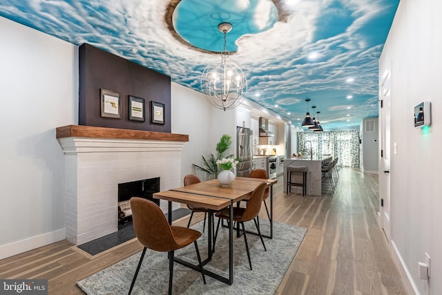 dining space with light wood-type flooring, recessed lighting, a fireplace, baseboards, and a chandelier