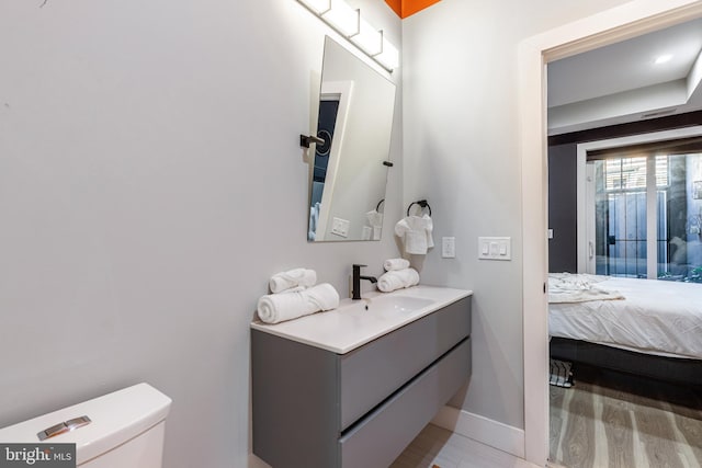 bathroom featuring baseboards, toilet, vanity, wood finished floors, and ensuite bath