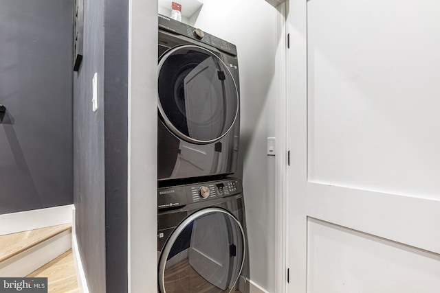 washroom with stacked washer and clothes dryer, wood finished floors, and laundry area