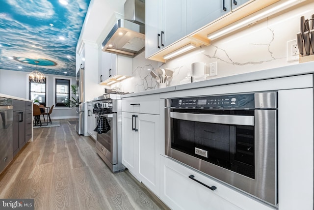 kitchen featuring stainless steel appliances, light wood finished floors, white cabinets, and wall chimney range hood