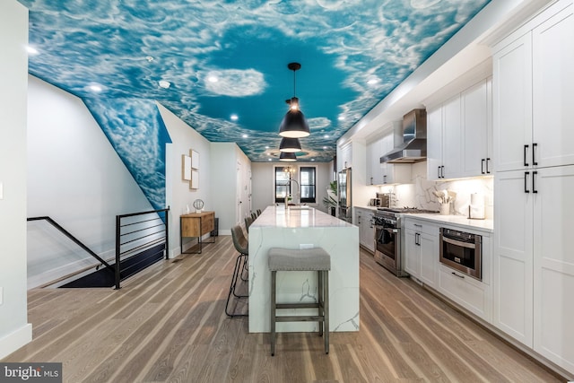 kitchen featuring stainless steel stove, wall chimney range hood, light wood-style floors, and white cabinets