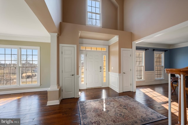 entrance foyer with a wainscoted wall, dark wood-style flooring, ornate columns, and ornamental molding