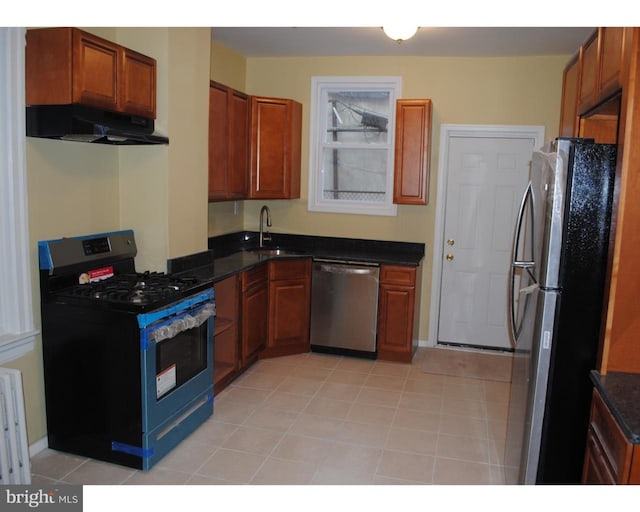 kitchen with under cabinet range hood, light tile patterned floors, brown cabinets, appliances with stainless steel finishes, and a sink