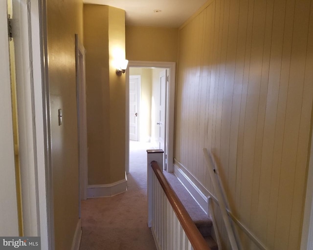 hallway with baseboards, an upstairs landing, wooden walls, and carpet flooring