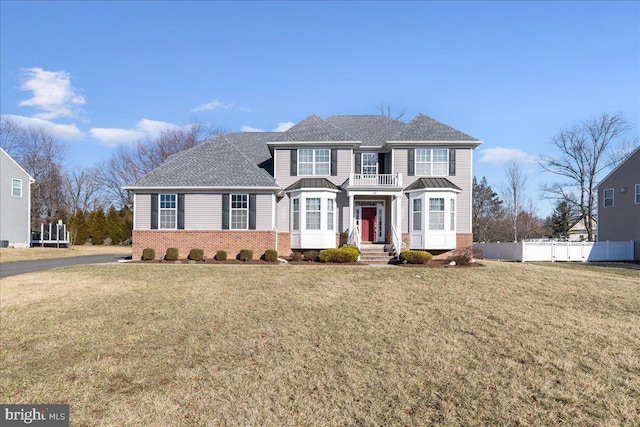 traditional home with a front yard, a balcony, fence, and brick siding