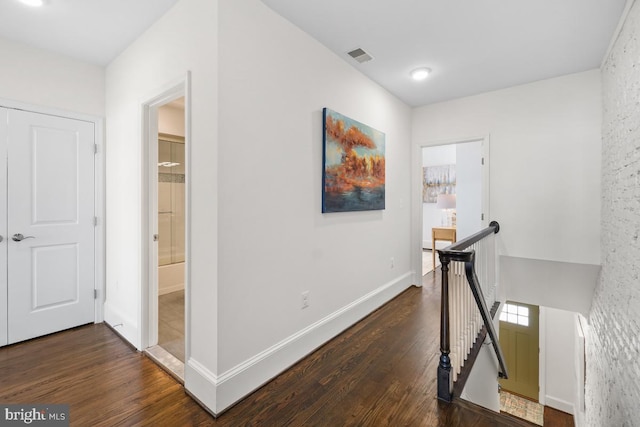 hall with baseboards, visible vents, dark wood-style floors, and an upstairs landing