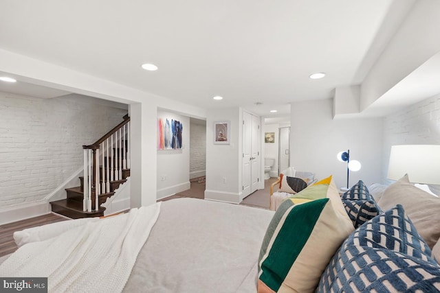 bedroom featuring baseboards, recessed lighting, wood finished floors, and brick wall