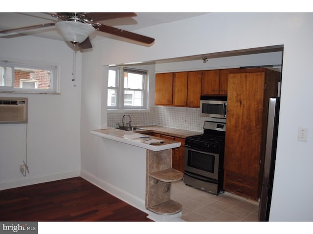 kitchen with brown cabinets, a sink, backsplash, stainless steel appliances, and light countertops